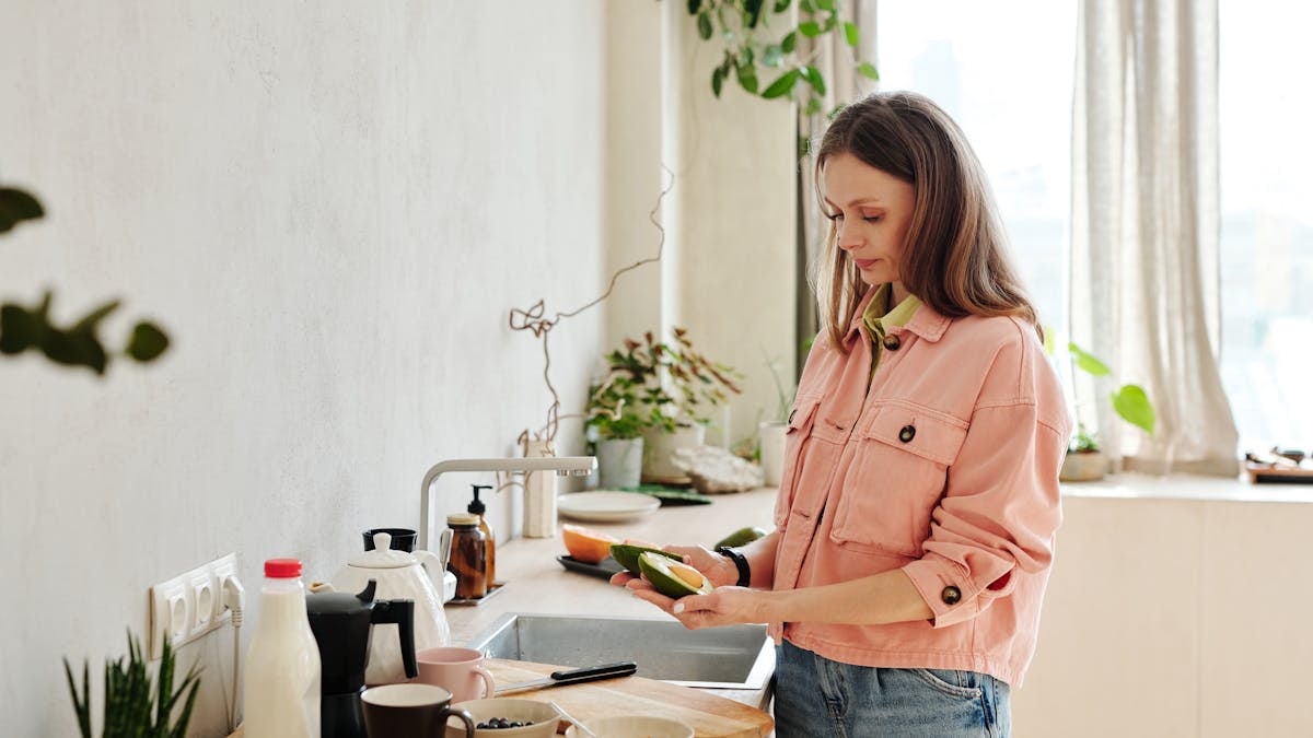 Woman preparing avocado in a modern kitchen with natural light.