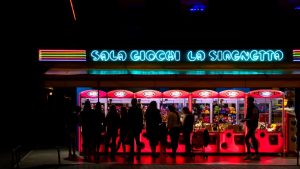 People enjoying a neon-lit arcade at night in Lido di Jesolo, Italy.
