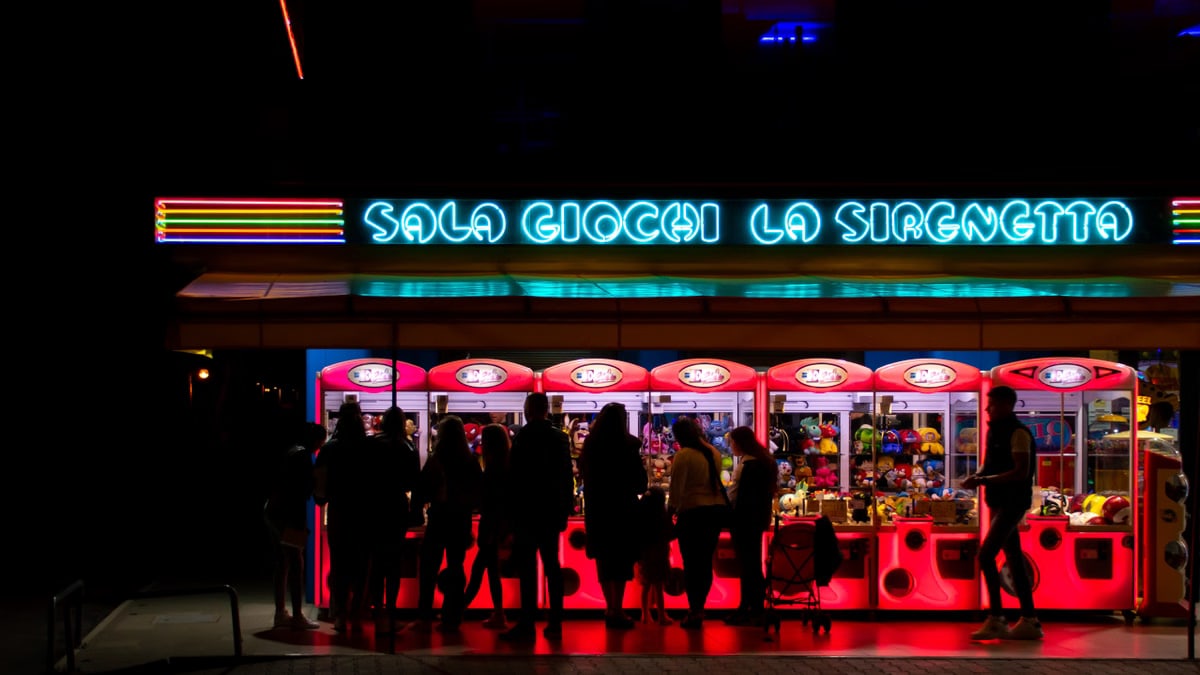 People enjoying a neon-lit arcade at night in Lido di Jesolo, Italy.
